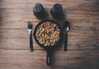 棕色木桌上叉子和勺子旁的黑色盘子里的熟食
